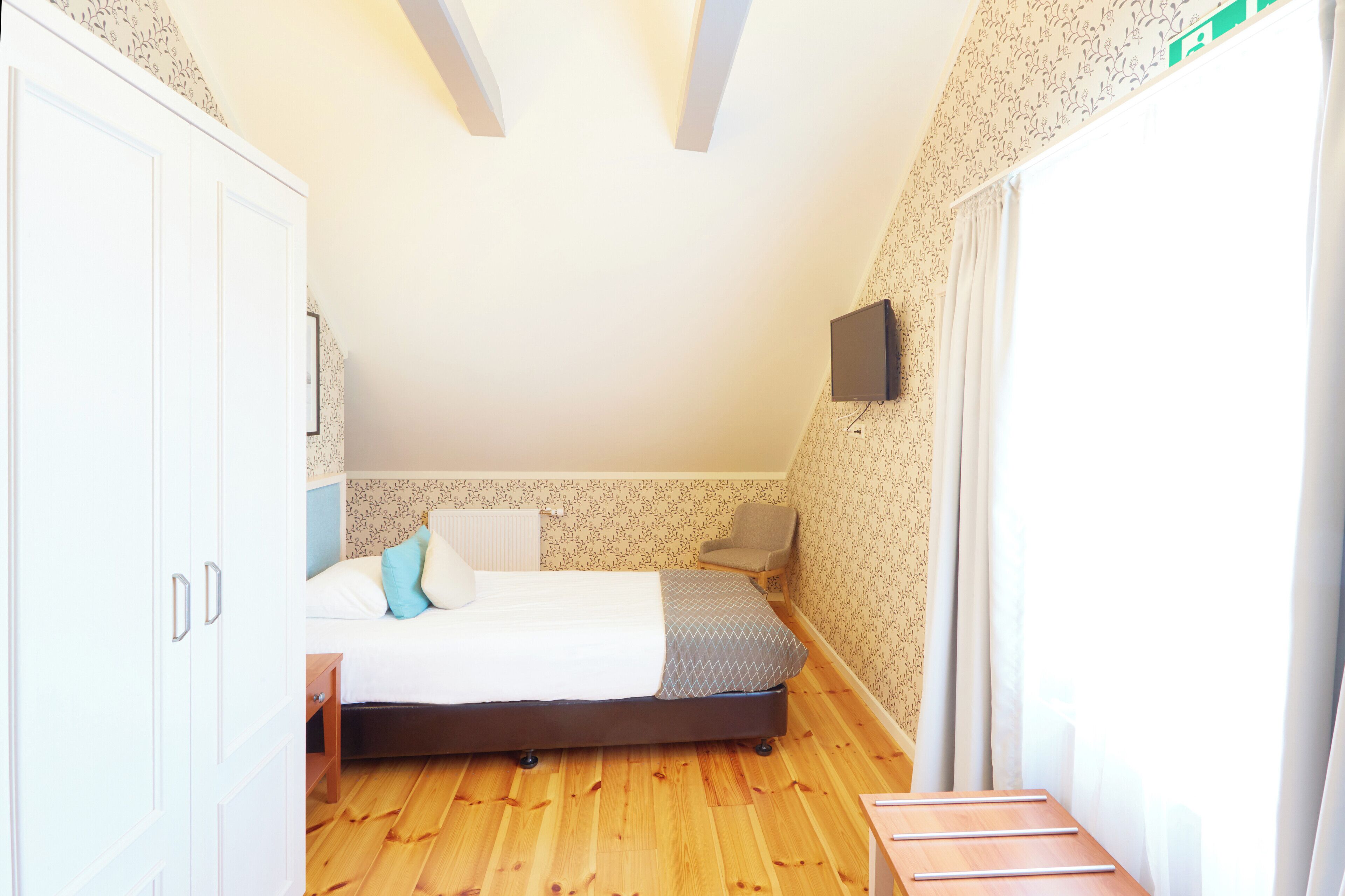A bedroom with a bed, a chair, a TV, and a wardrobe.