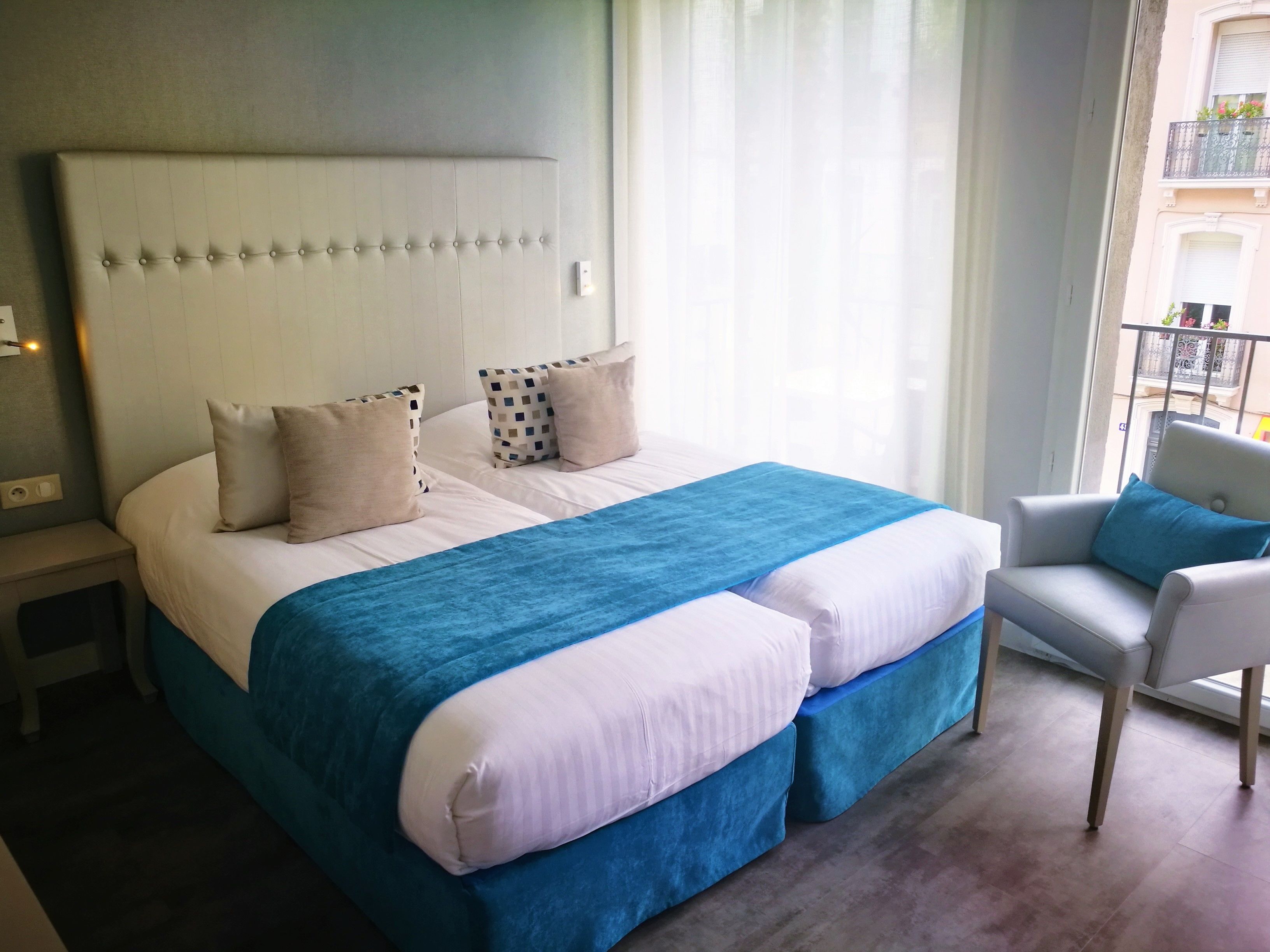 A hotel room with a large bed, a nightstand, a chair, and a window with curtains.
