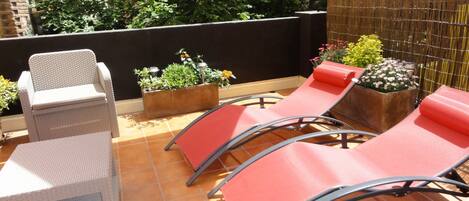 A terrace with outdoor seating, potted plants, and a view of greenery.