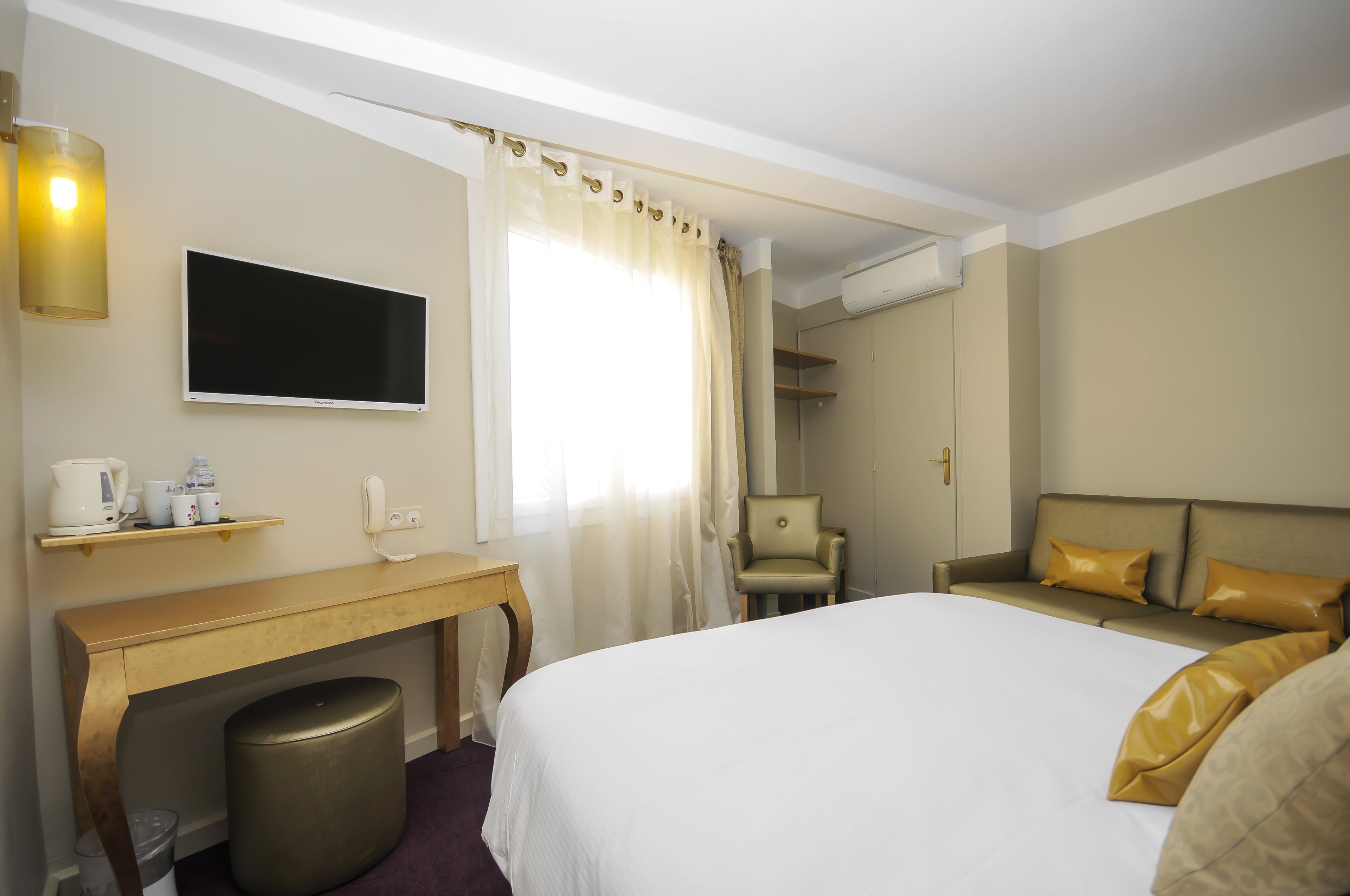 Una habitación de hotel con una cama, un escritorio con silla, un televisor y una ventana con cortinas.