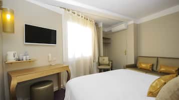 Una habitación de hotel con una cama, un escritorio con silla, un televisor y una ventana con cortinas.