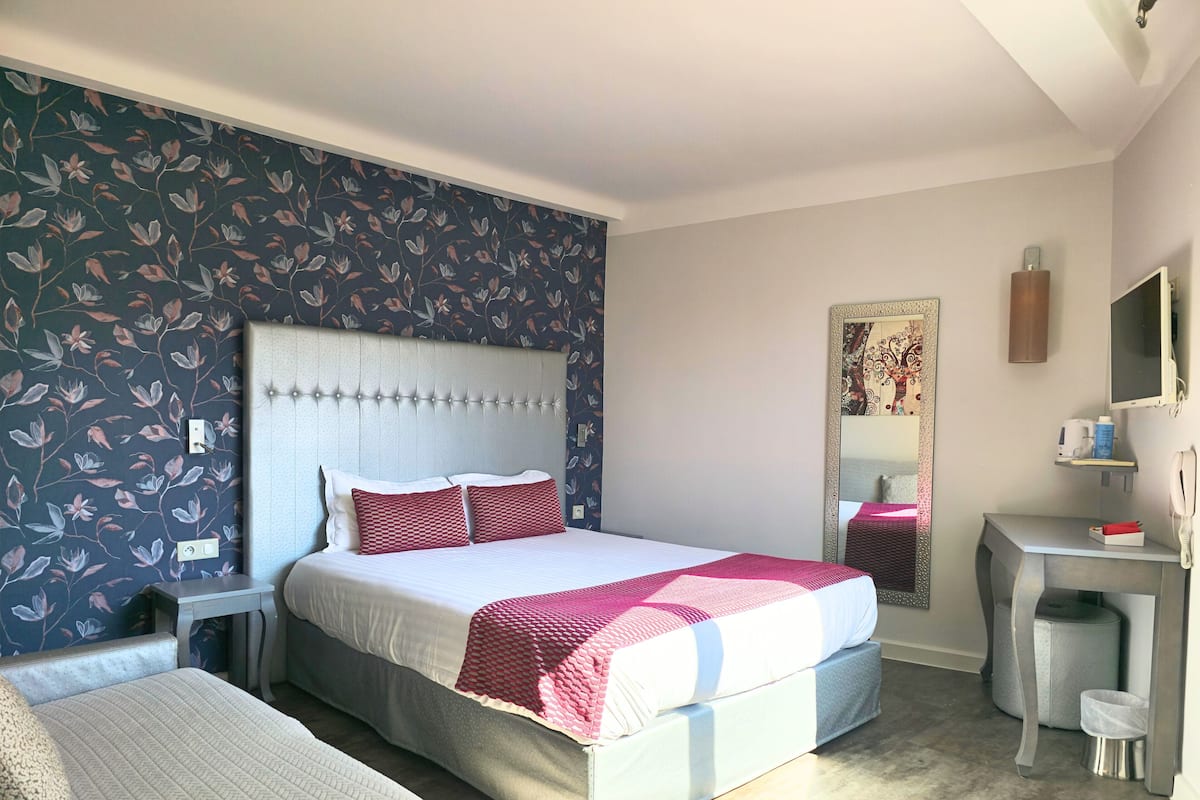 Hotellihuone, jossa on sänky, yöpöydät, työpöytä ja peili.