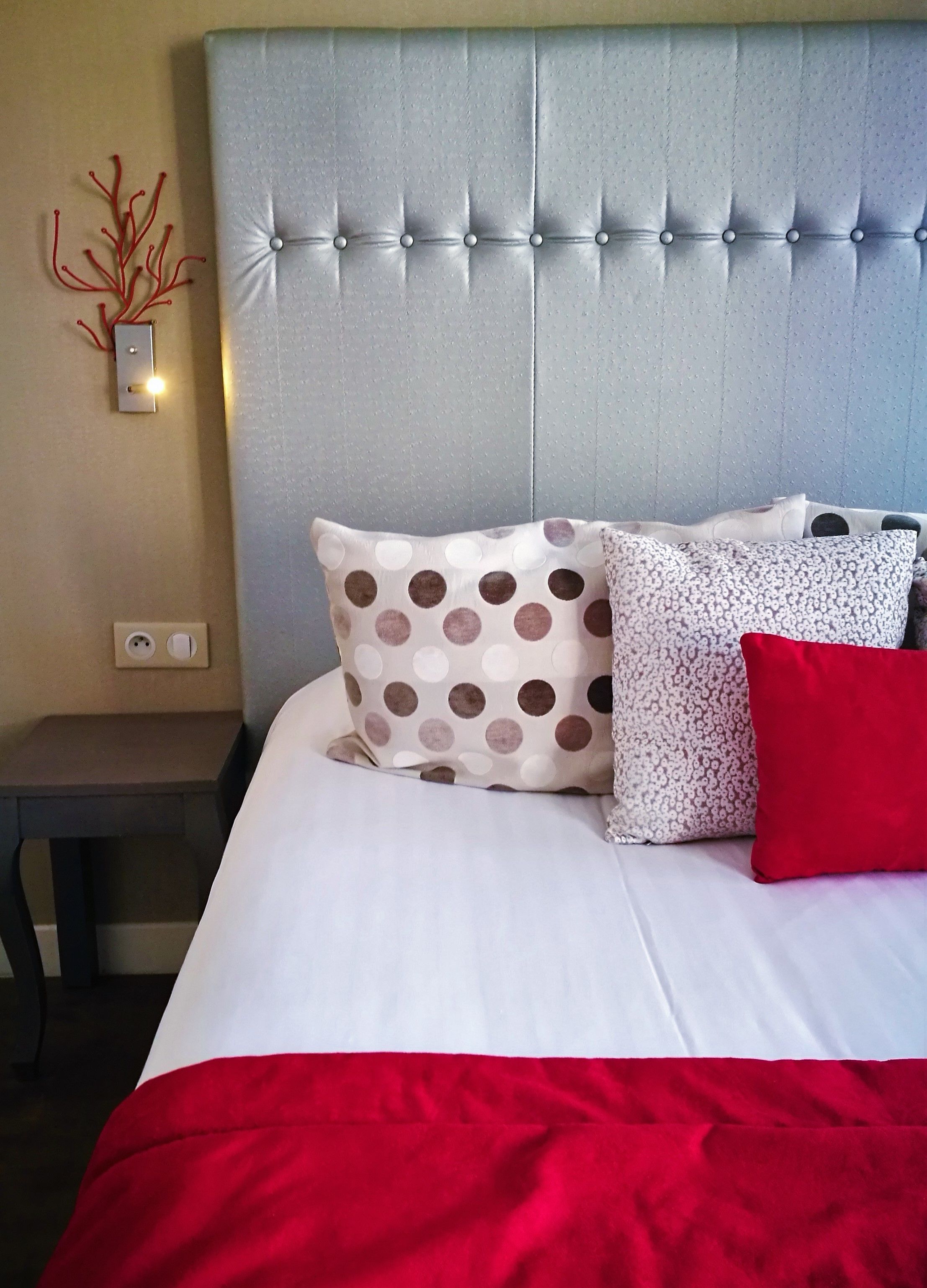 A neatly made bed with a grey headboard, white and red bedding, and patterned pillows.
