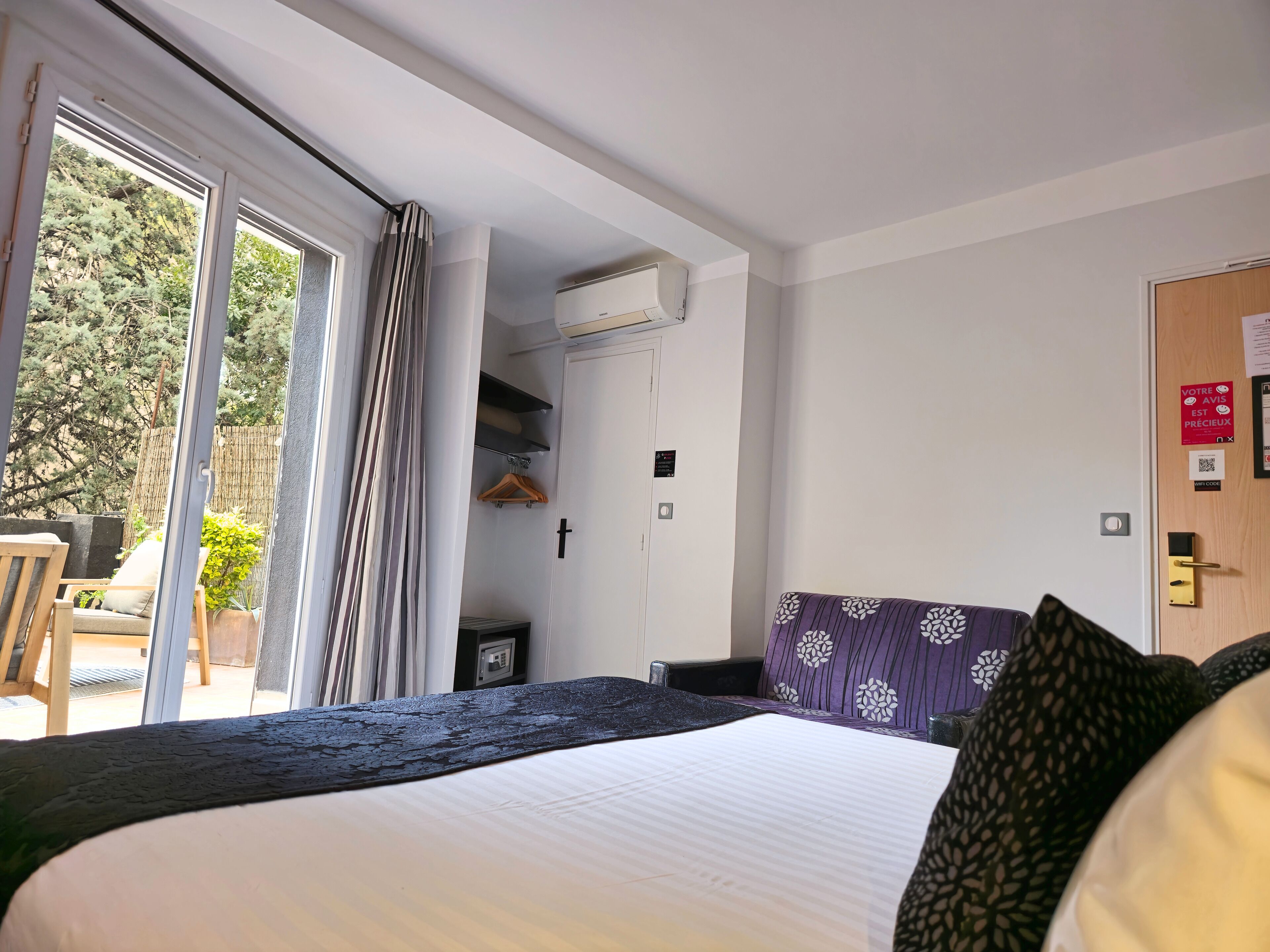 A hotel room with a bed, a desk, and a chair. There is a sliding glass door leading to an outdoor area with a table and chairs.