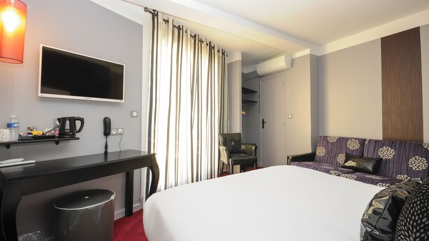 A hotel room with a bed, a desk with a telephone and a coffee maker, a chair, and a TV mounted on the wall. - NYX Hotel (Perpignan)