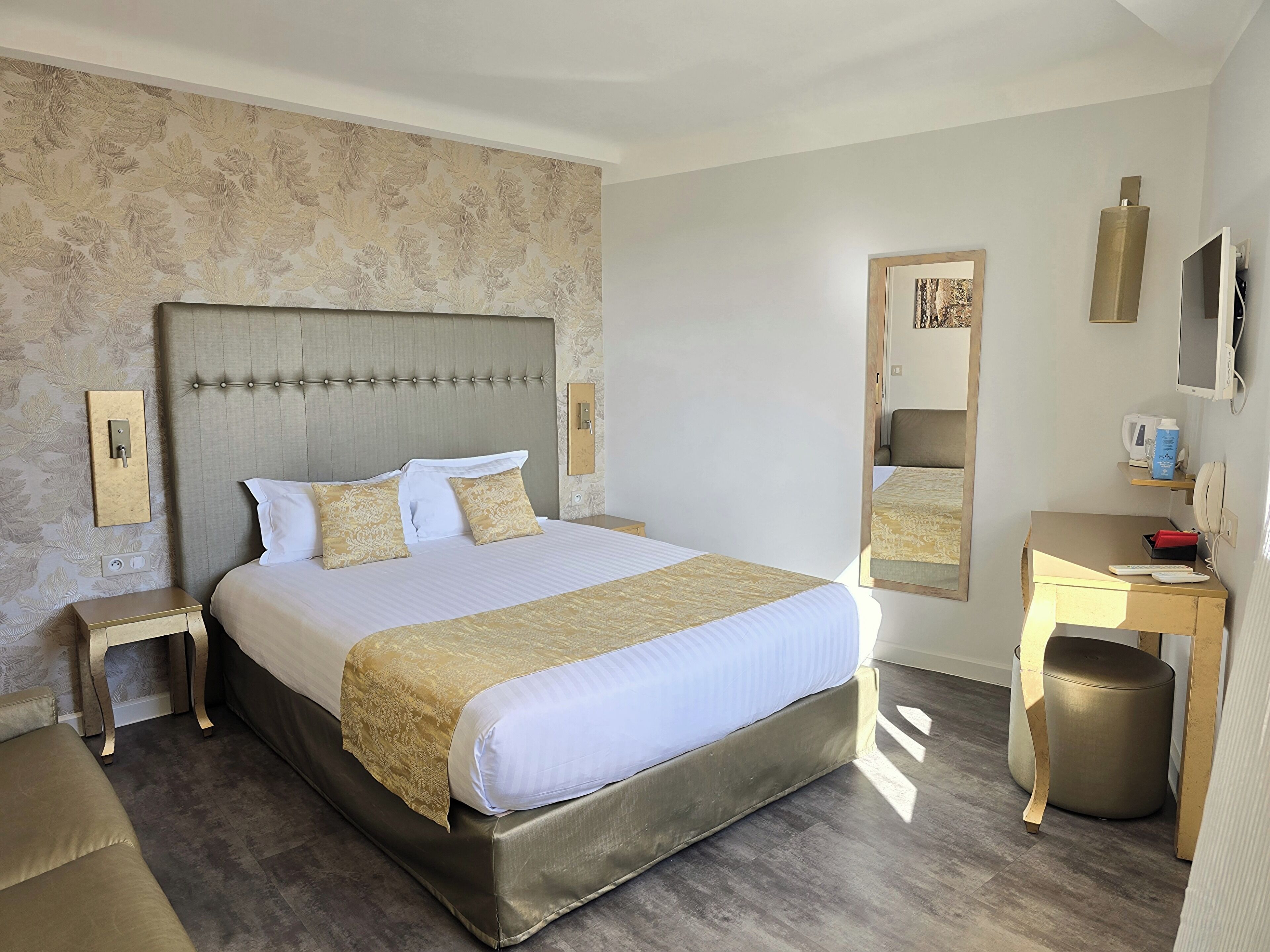 Ein Hotelzimmer mit einem großen Bett, Nachttischen, einem Schreibtisch, einem Spiegel und einem Fernseher.