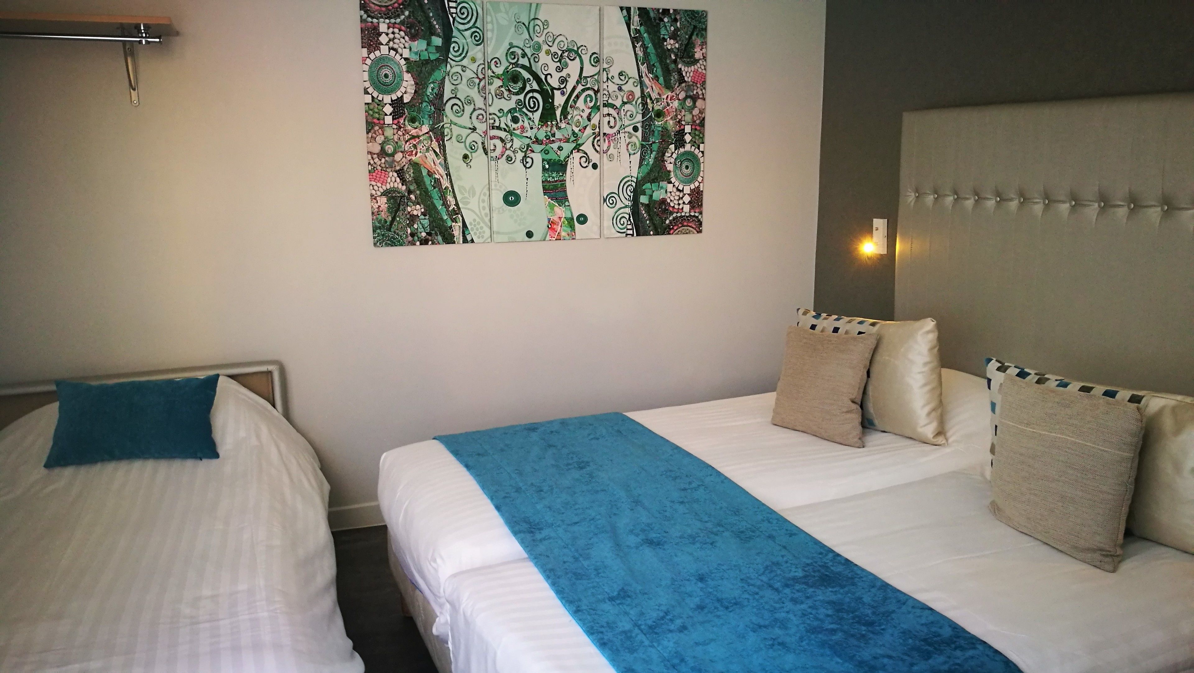 A hotel room with two beds, a blue throw blanket, and a decorative tapestry on the wall.