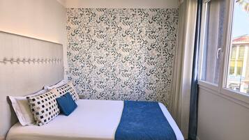Une chambre d’hôtel avec un lit, une tête de lit, une fenêtre avec des rideaux et une vue sur les bâtiments environnants.