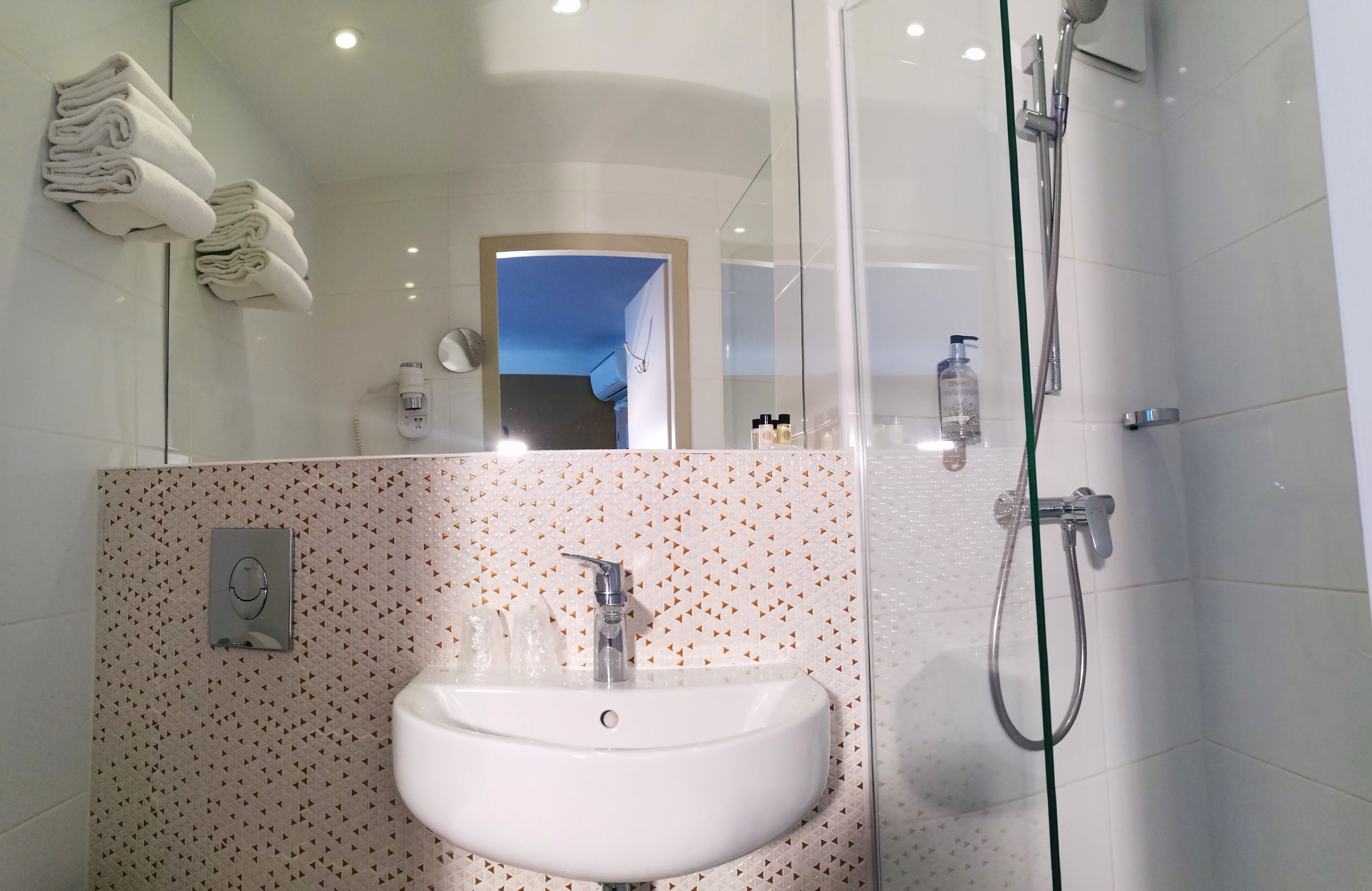 A modern bathroom with a white sink, a glass shower enclosure, and neatly folded towels on a rack.