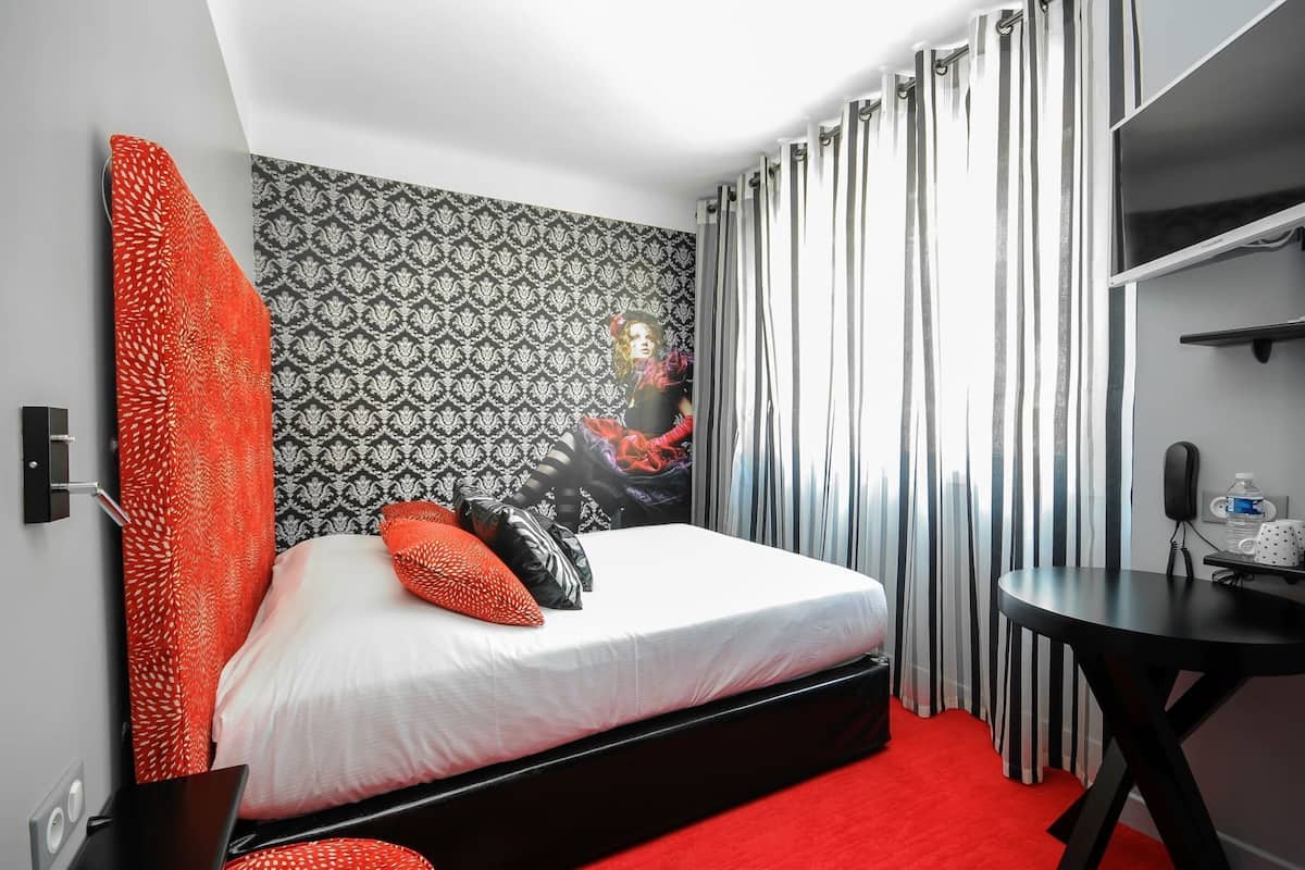 Hotellihuone, jossa on sänky, työpöytä, puhelin ja vesipullo.