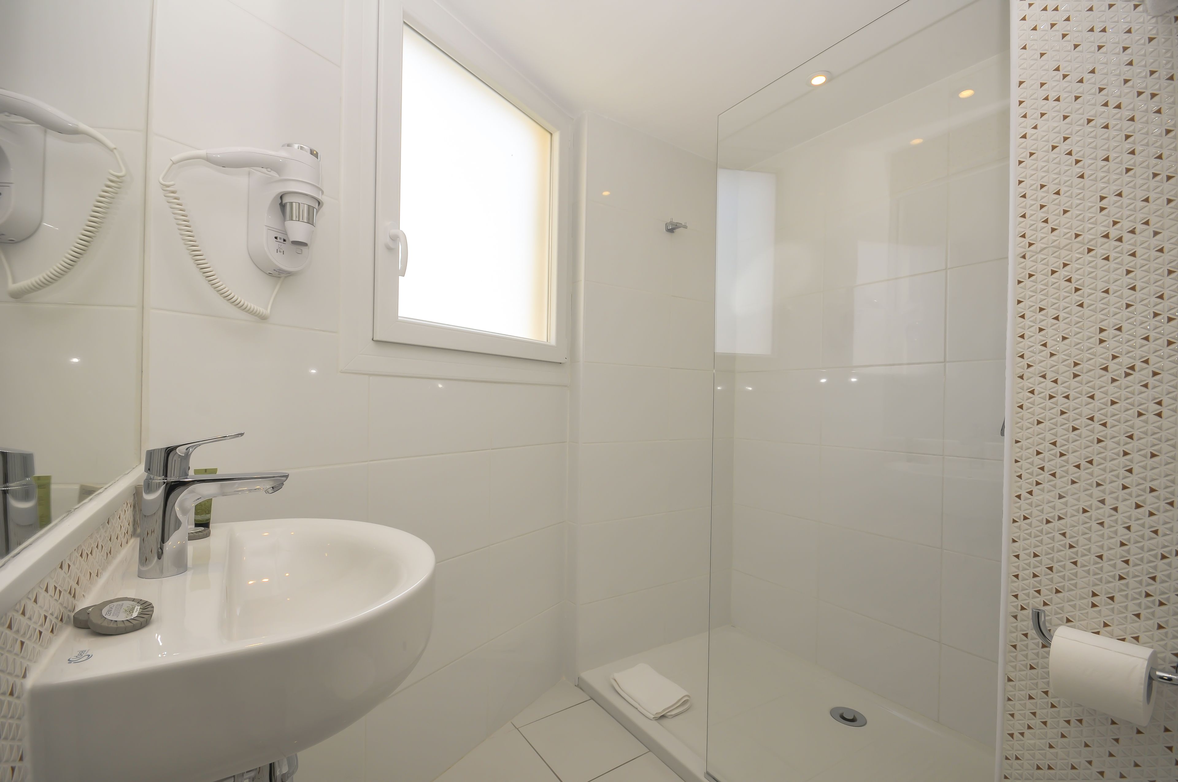 A bathroom with a white sink, a hairdryer, and a shower with a patterned wall.