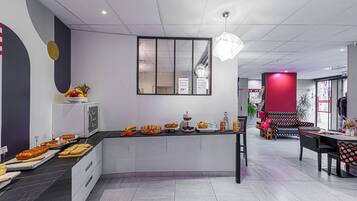 A modern kitchen with a central island, a dining area with a red accent wall, and a view into the adjacent room.