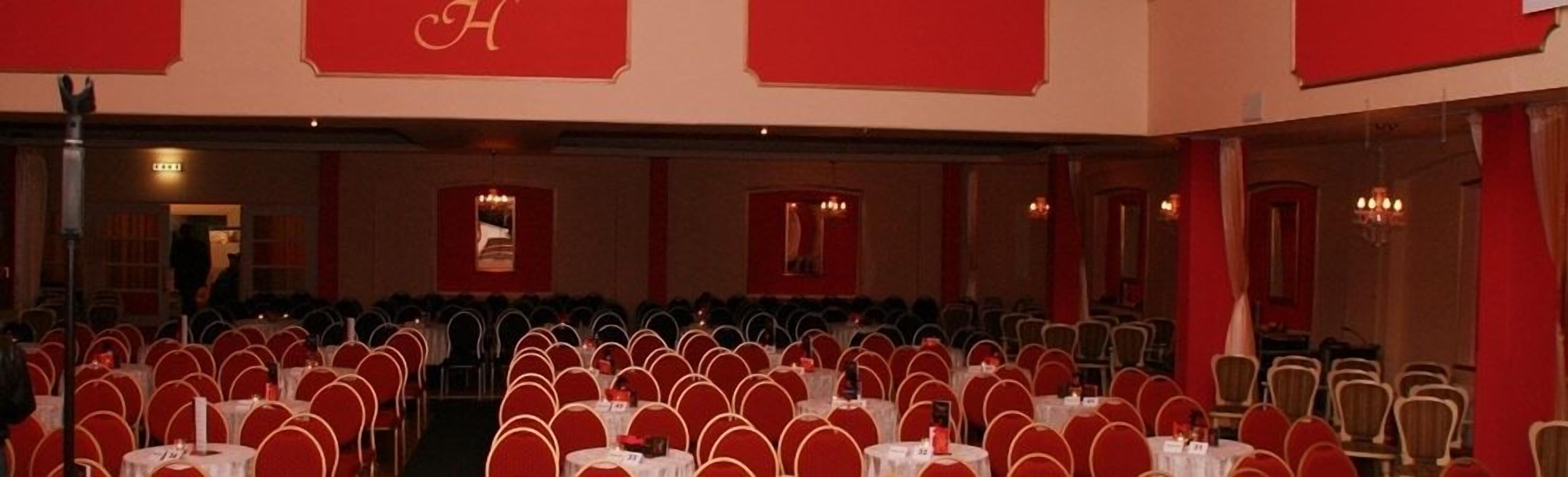 Ein Konferenzraum mit Tischen und Stühlen, roten Akzenten und Kronleuchtern.