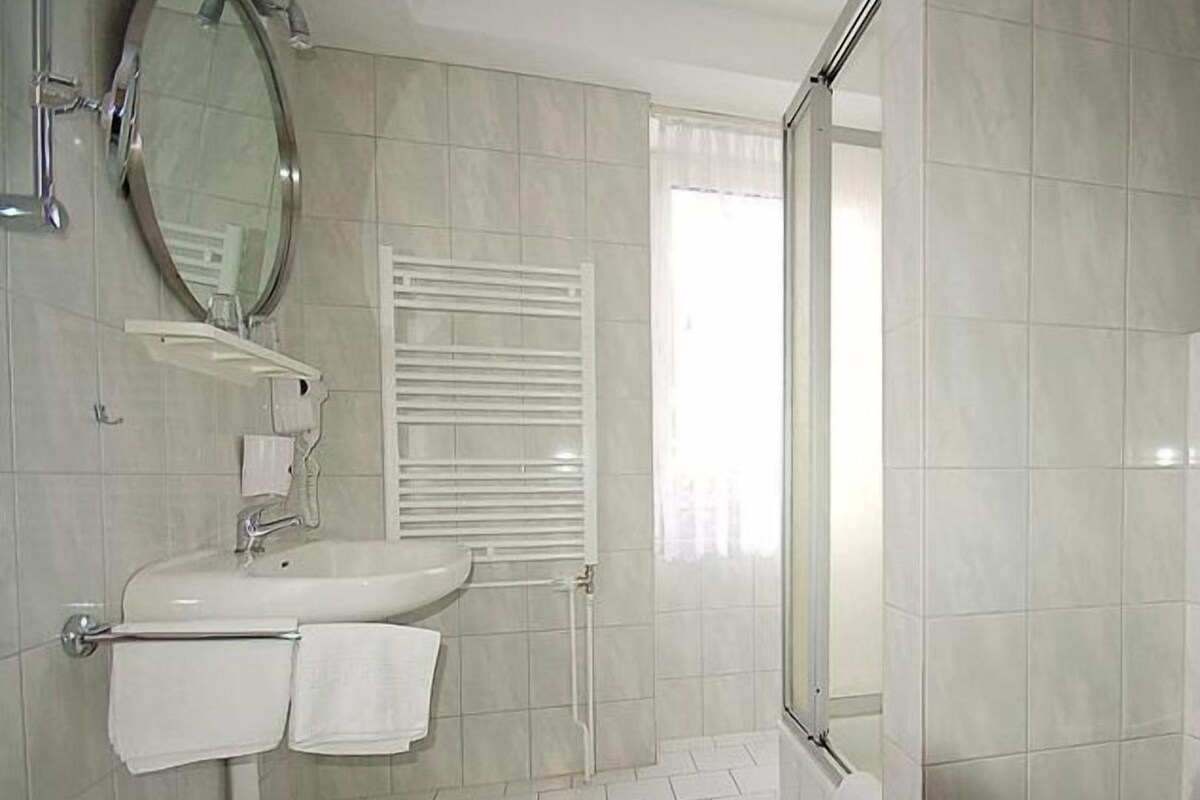 A bathroom with a sink, mirror, towel rack, and a shower area.