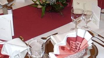 Una mesa dispuesta para un evento formal con servilletas blancas y rosas, cristalería transparente y cubiertos dorados.