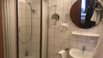 Une salle de bain d’hôtel avec une douche en verre, un lavabo, un miroir et un porte-serviettes.