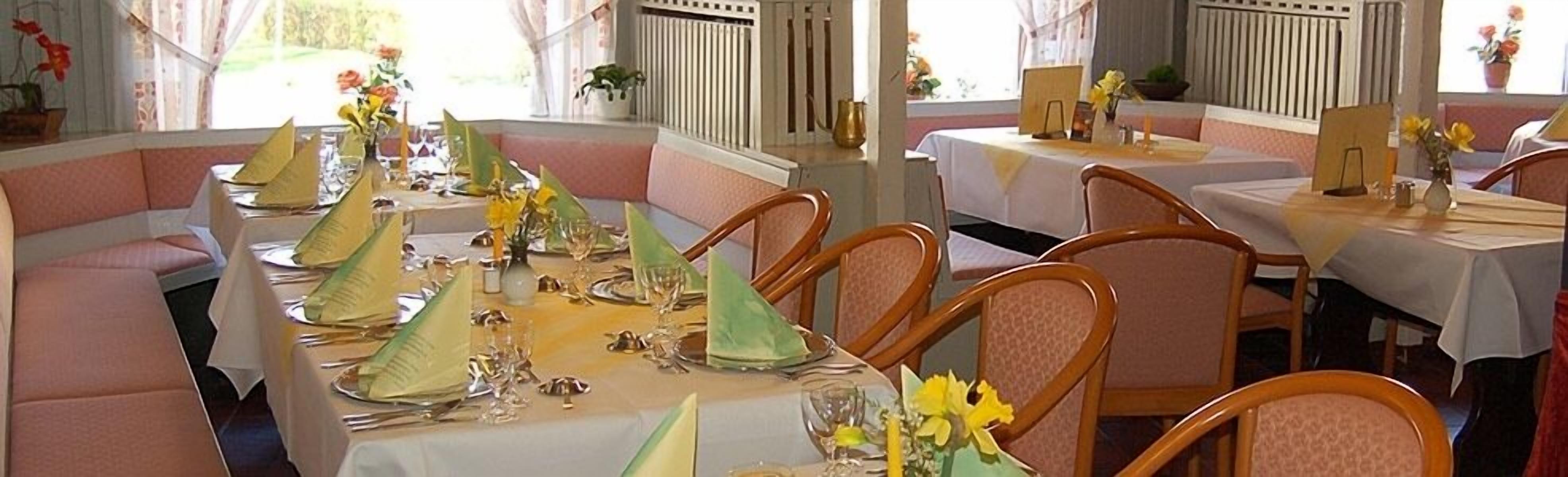 Een restaurant met ronde tafels gedekt voor diner, met groene servetten en gele bloemen.