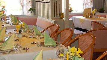 Een restaurant met ronde tafels gedekt voor diner, met groene servetten en gele bloemen.
