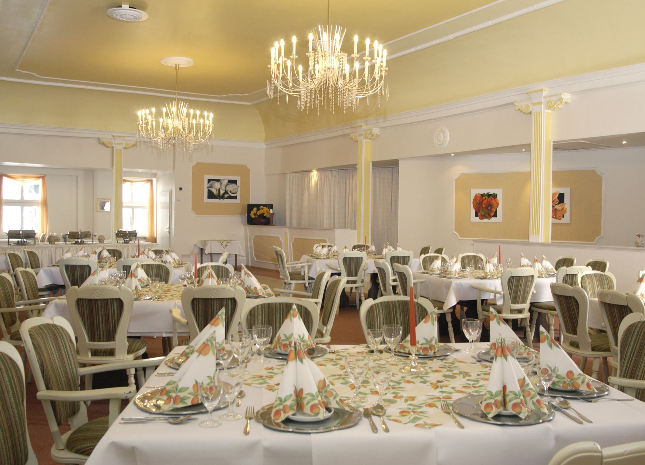 Un salón de banquetes con varias mesas dispuestas para comer, con manteles florales y elegantes candelabros.