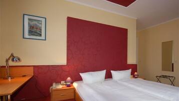 Een hotelkamer met een bed, een bureau, een stoel, een lamp, een nachtkastje en een aan de muur hangend schilderij.