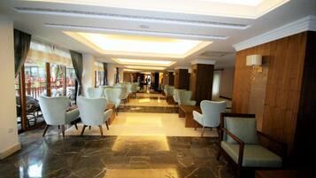 A hotel lobby with a marble floor, light-colored chairs, and a wooden wall with a lamp.