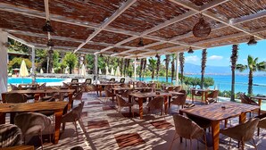 A covered outdoor dining area with tables and chairs, overlooking a pool and the sea. - Club & Hotel Letoonia (Fethiye)