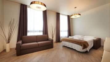A modern hotel room with a wooden floor, a brown sofa, a bed with white bedding, and two pendant lights.
