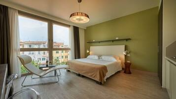 Quarto de hotel com cama, uma cadeira, uma mesa e uma grande janela com vista para a cidade.