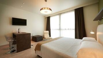 A hotel room with a bed, a desk with a chair, a TV, and a window with curtains.