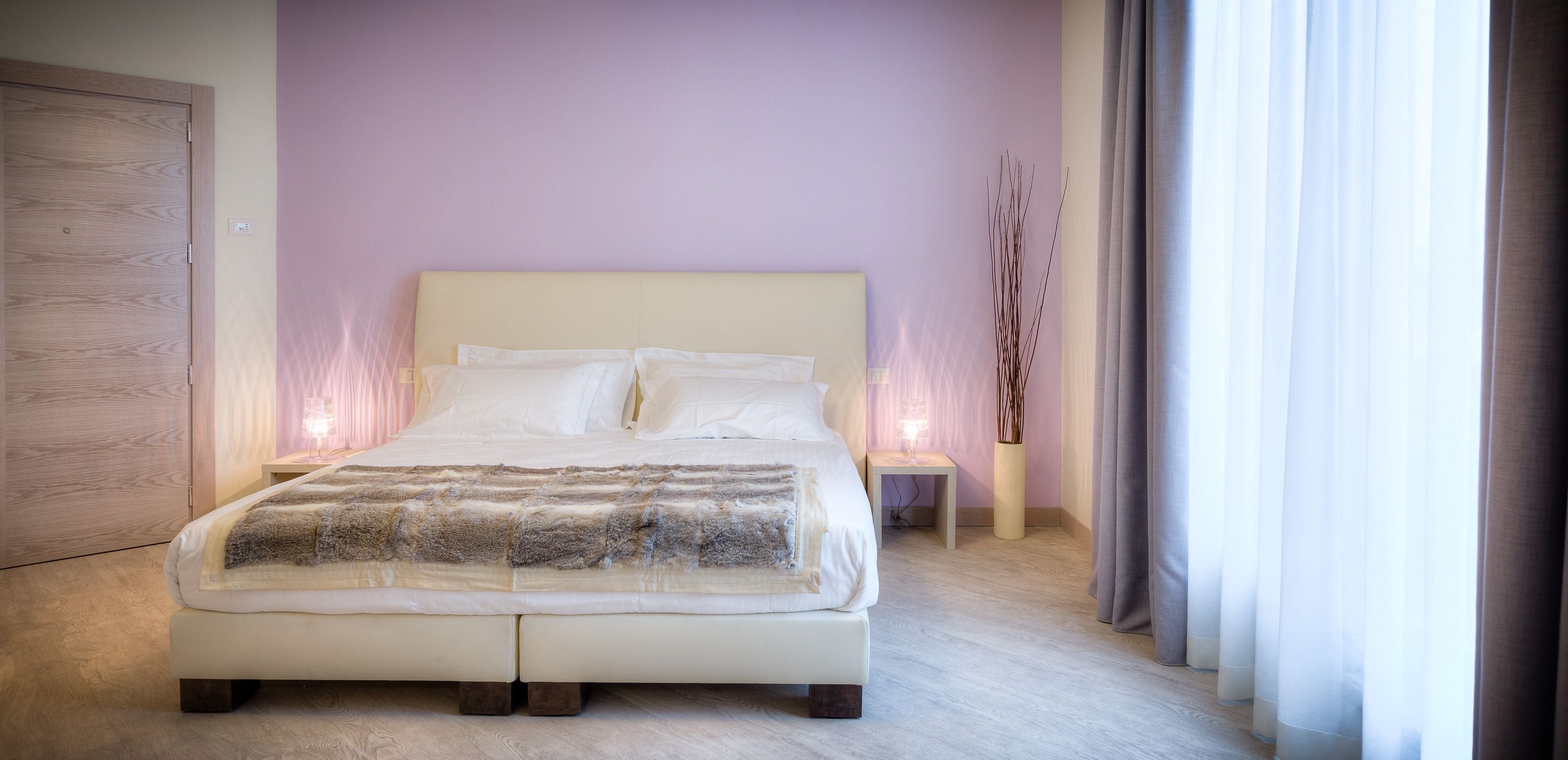 A bedroom with a large bed, two bedside tables, a nightstand, and a window with curtains.