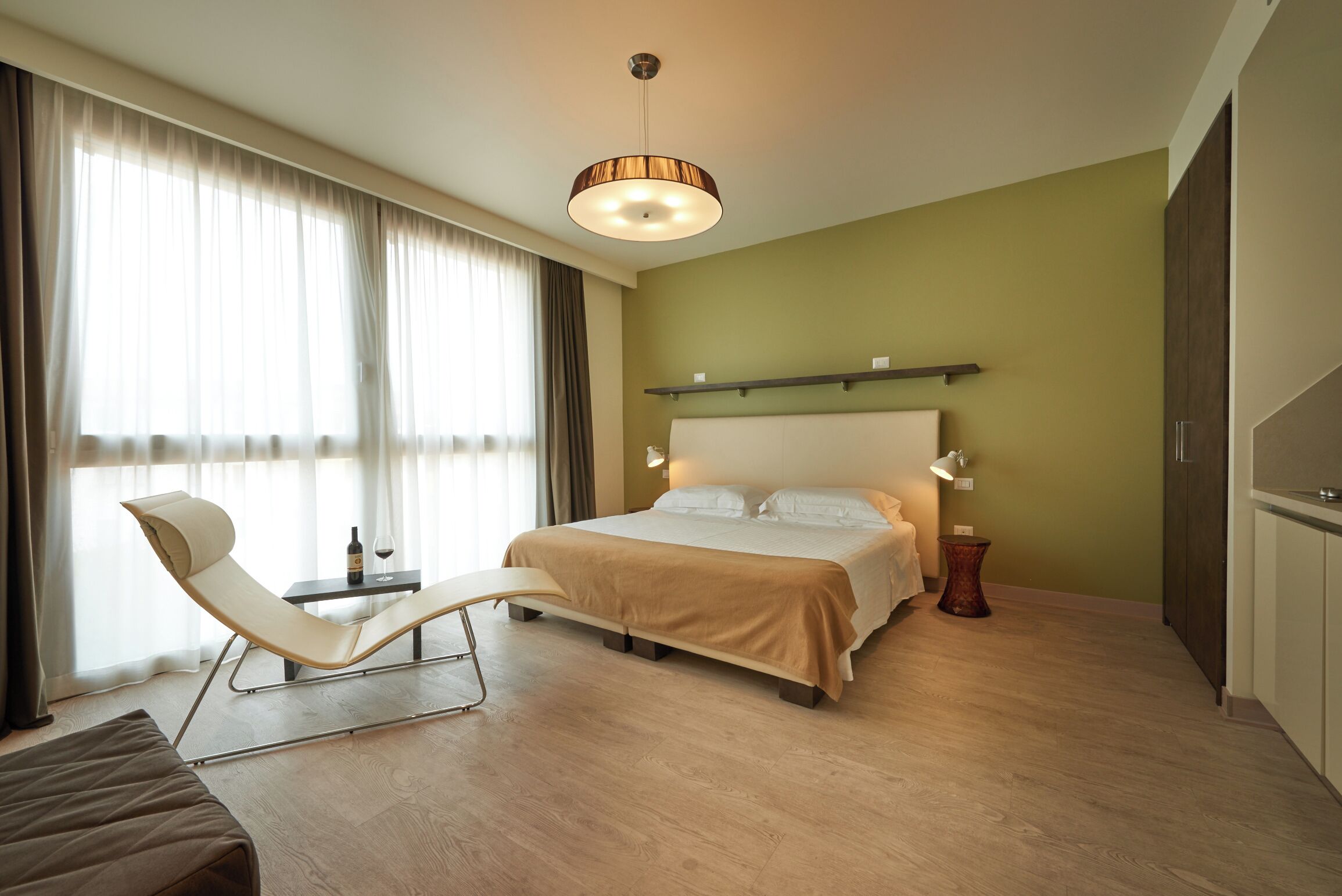 A hotel room with a bed, a chair, a bedside table, a lamp, and a window with curtains.
