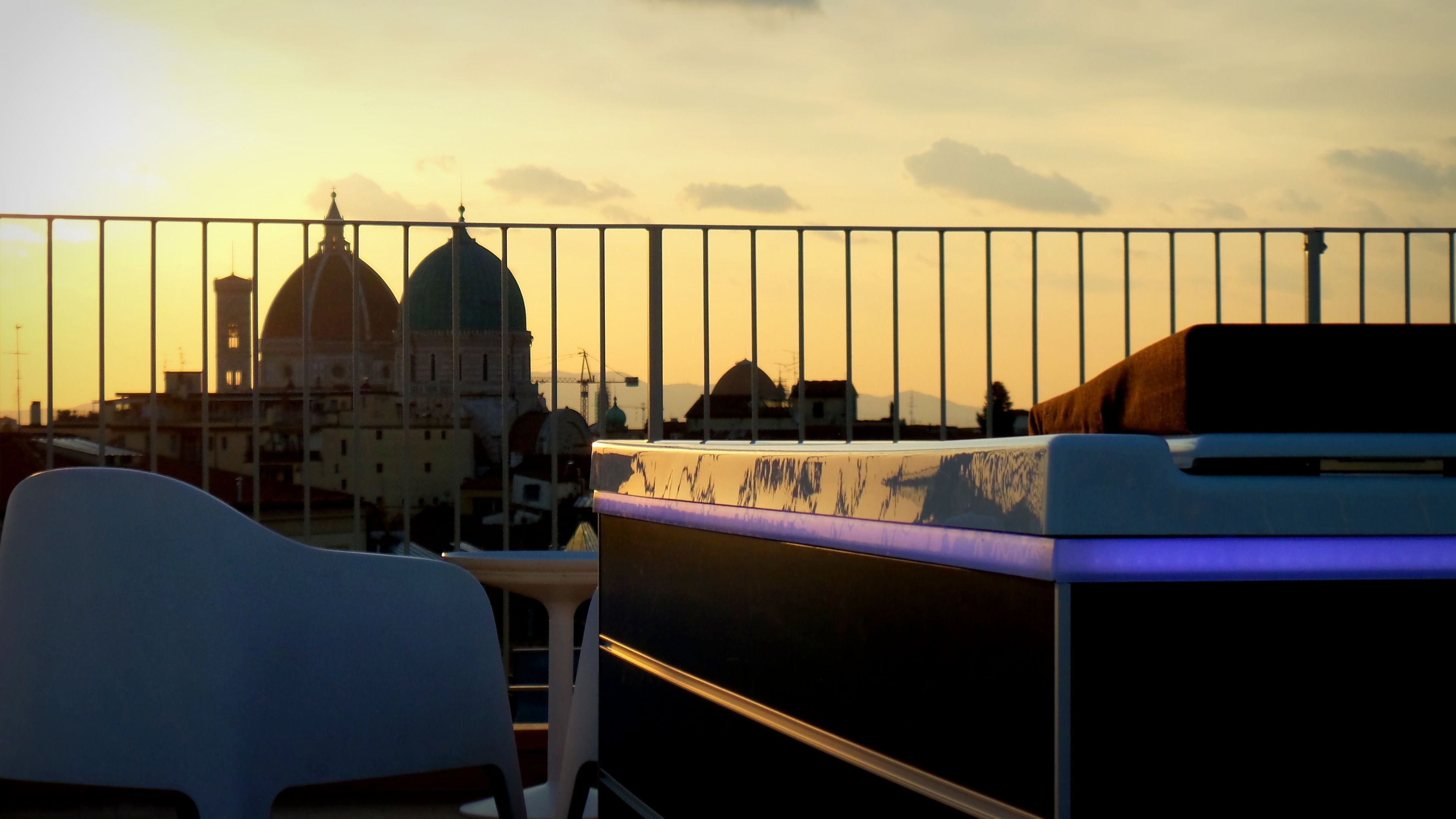 A balcony with a view of a cityscape at sunset, including a prominent building with domes.