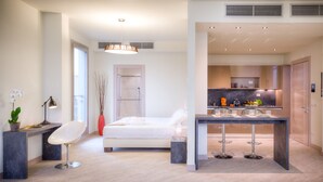 A modern hotel room with a bed, a desk with a chair, a dining area with a table and chairs, and a kitchen in the background. - Forte16 View & Spa (Florence)