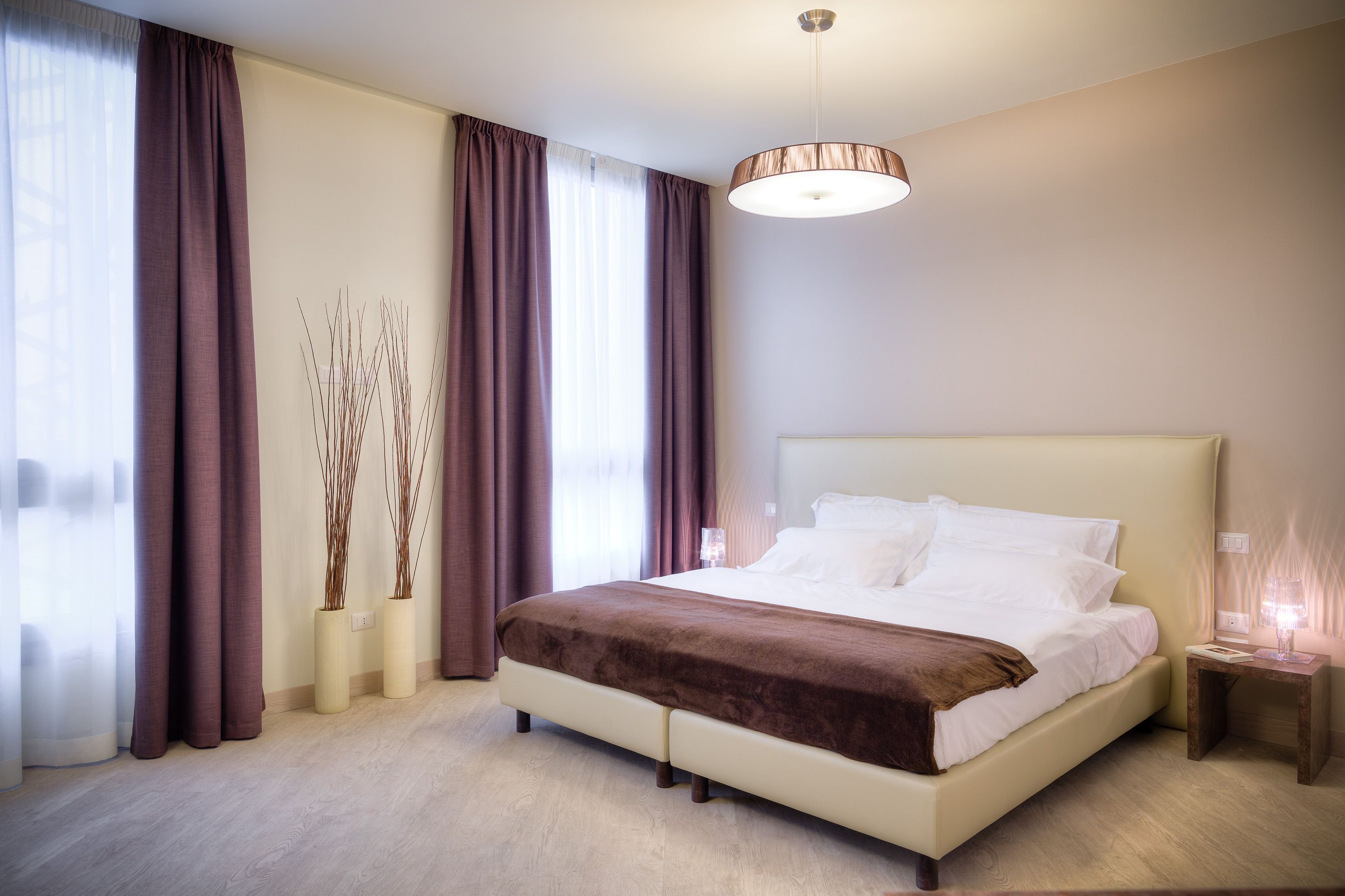 A neatly arranged bedroom with a large bed, a bedside table, and a hanging light fixture.