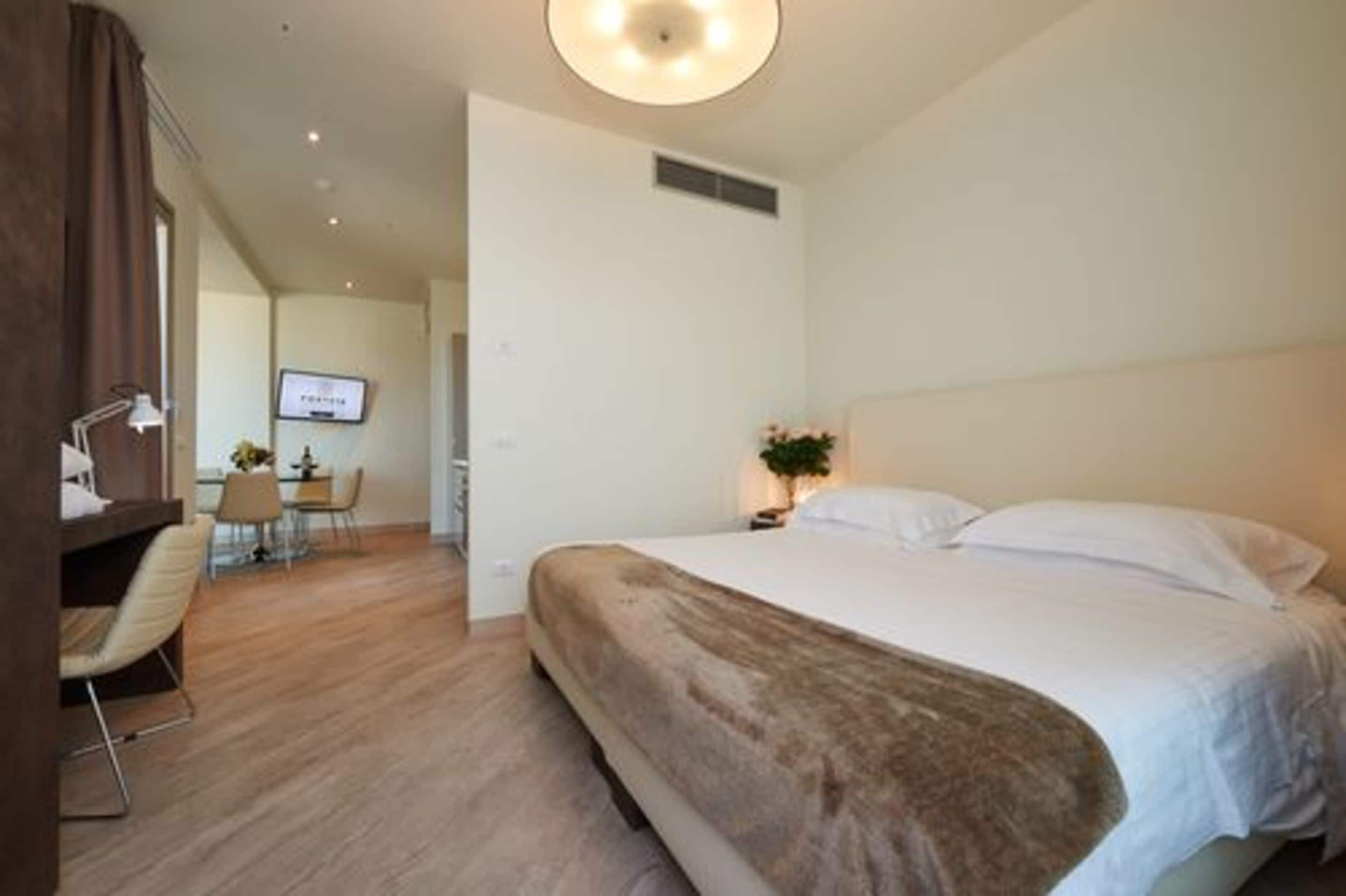 Une chambre d’hôtel avec un grand lit, un bureau avec une chaise, une télévision et une plante.