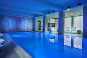 Una piscina interior amb aigua cristal·lina, terra de rajola i algunes gandules al costat.