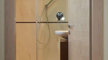 Ein Duschbereich mit Glaswänden, einer Handbrause und einem wandmontierten Wasserhahn.