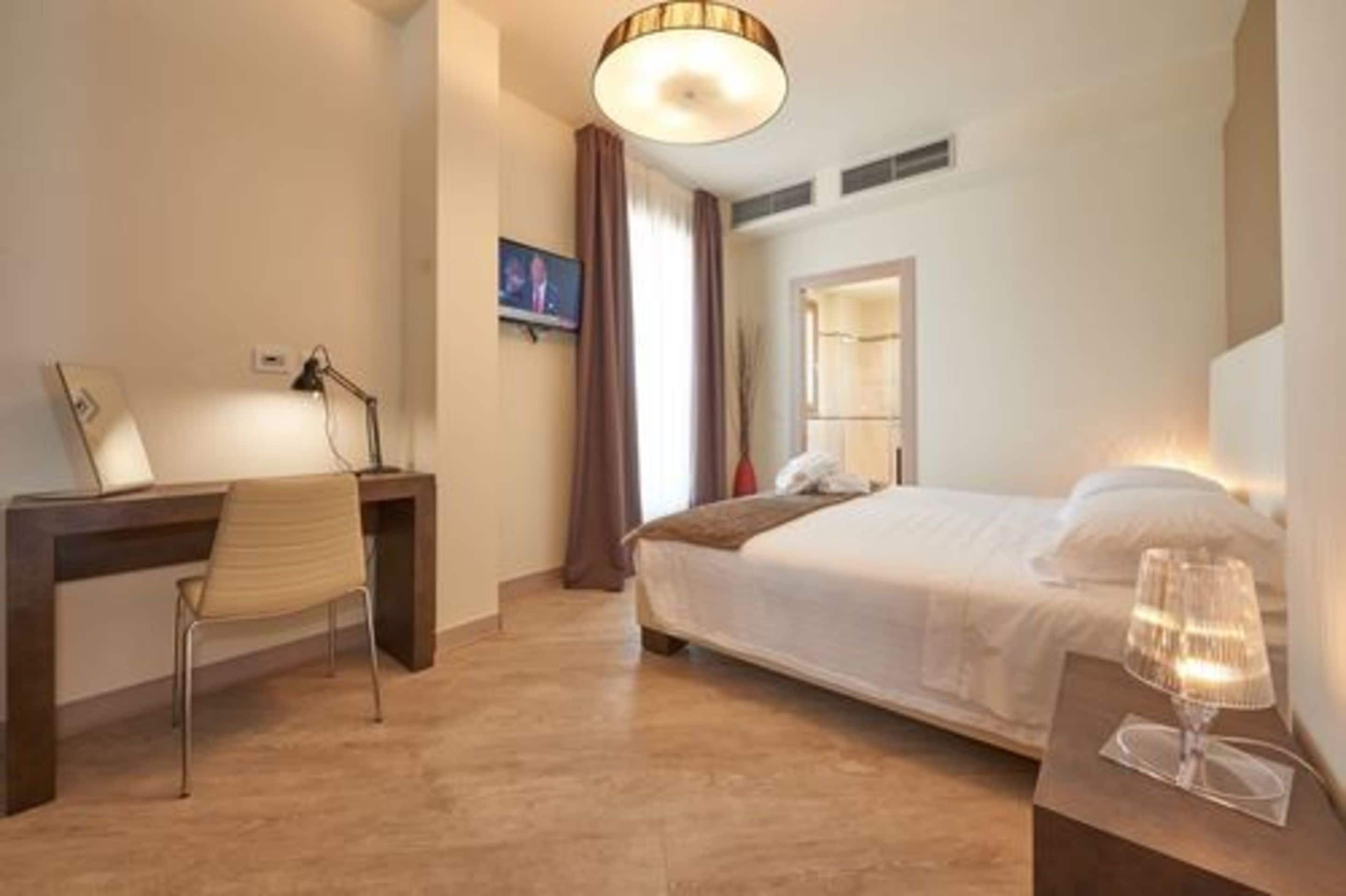 A hotel room with a bed, a desk, a chair, a lamp, and a television.