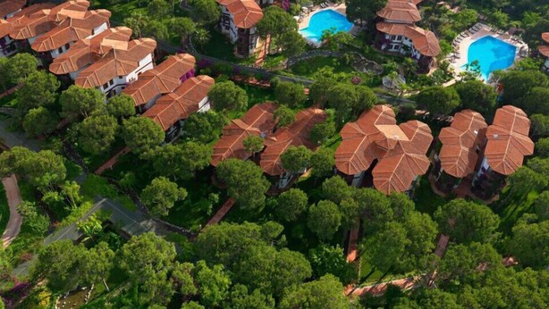 An aerial view of a residential area with multiple houses featuring red-tiled roofs, surrounded by lush greenery. - Selectum Family Resort Belek (Serik)
