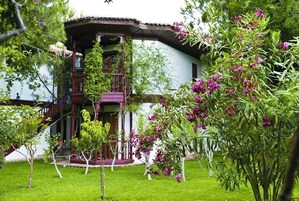 En traditionel bygning med en træbalkon, omgivet af frodig vegetation og blomstrende planter.
