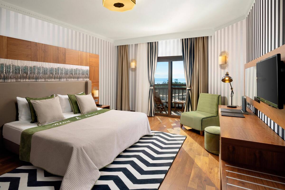 Une chambre d’hôtel avec un lit, un bureau, une télévision et un balcon offrant une vue.