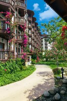 A pathway leading to a building with multiple balconies, surrounded by lush greenery and flowering plants.
