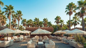 A beachside lounge with thatched umbrellas, wicker furniture, and palm trees. - Selectum Family Resort Belek (Serik)