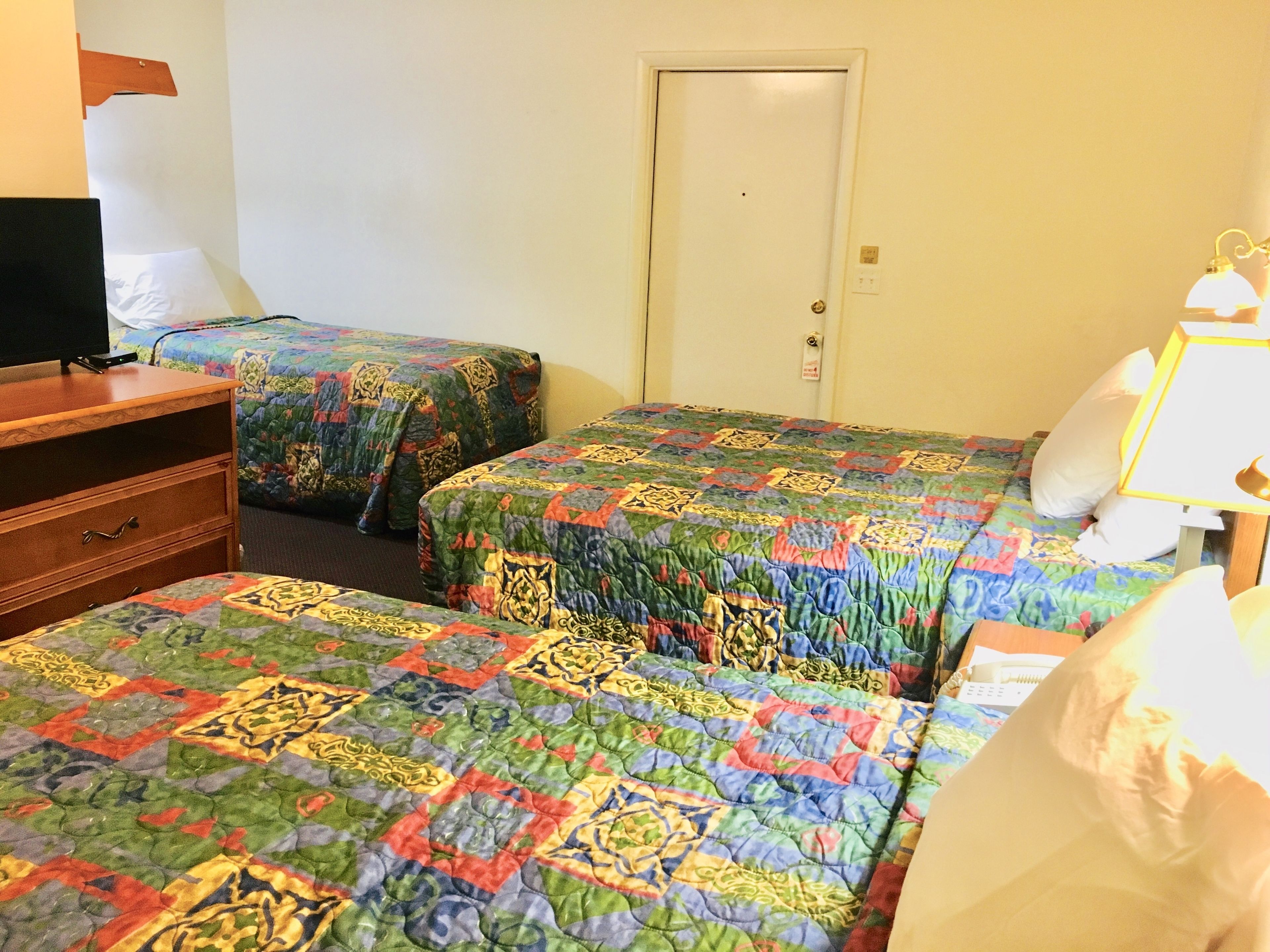 A hotel room with two beds, a wooden dresser, a television, and a door.