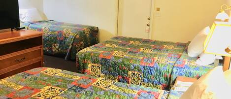 A hotel room with two beds, a wooden dresser, a television, and a door.