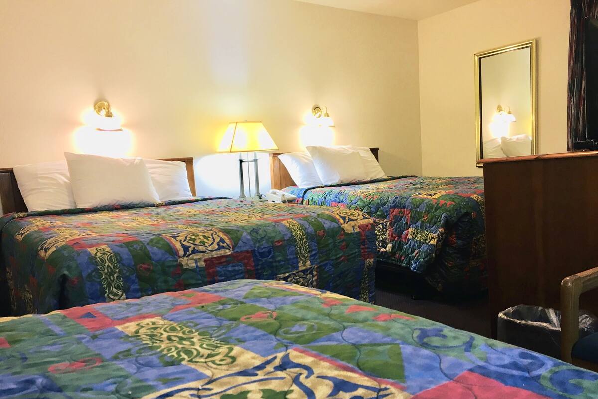 A hotel room with two beds, each with a colorful quilt, bedside lamps, and a mirror on the wall.