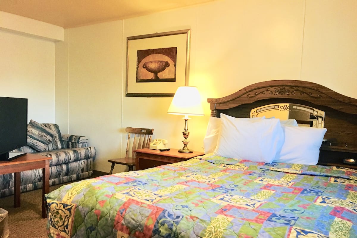 A hotel room with a bed, a television, a chair, a desk with a lamp, and a framed picture on the wall.