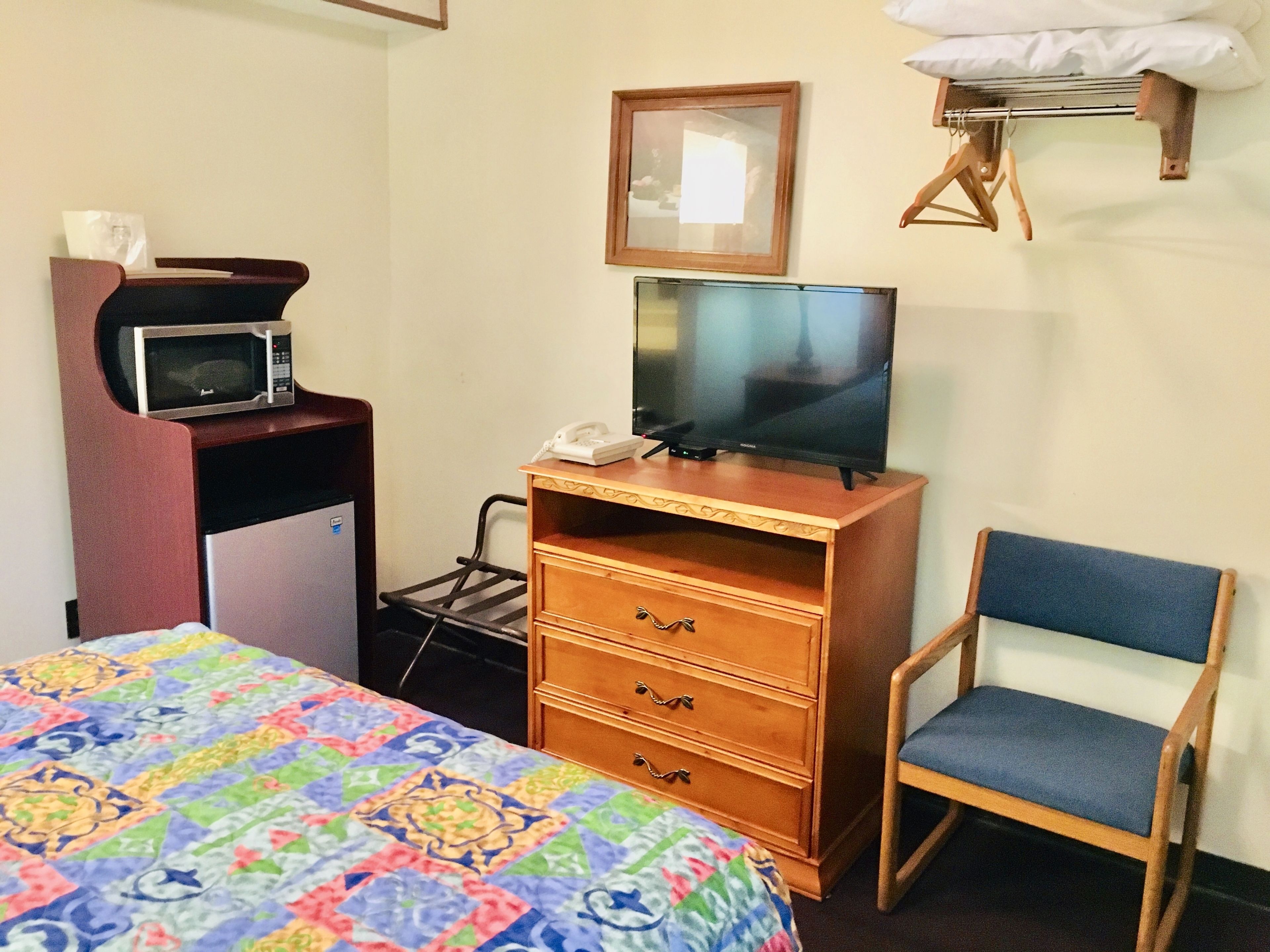 A hotel room with a bed, a wooden dresser with a television, a microwave, a phone, and a chair.