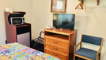 Une chambre d’hôtel comprenant un lit, une commode en bois avec un téléviseur, un four à micro-ondes, un téléphone et une chaise.
