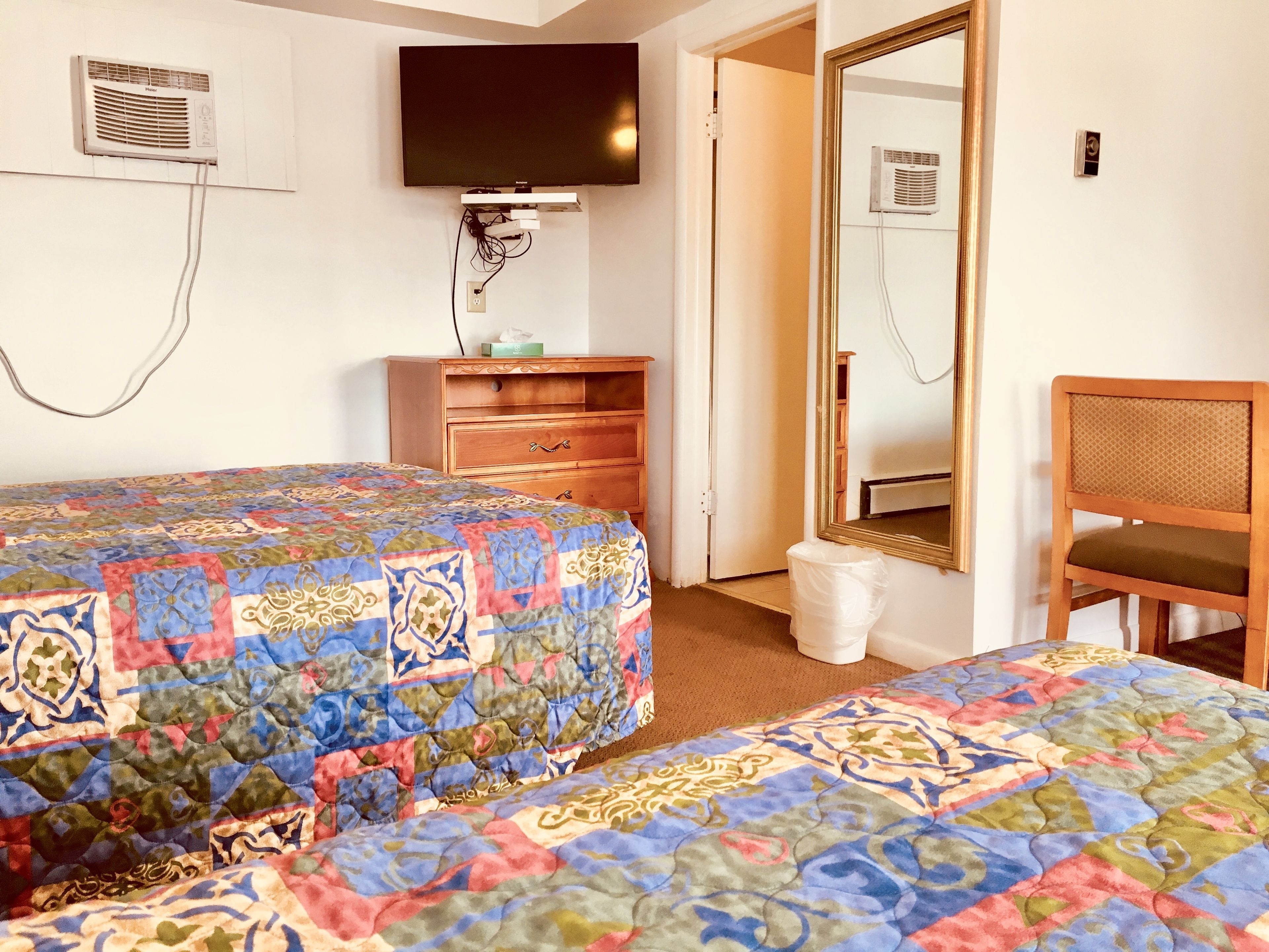 A hotel room with two beds, a wooden dresser, a television, a mirror, and a chair.